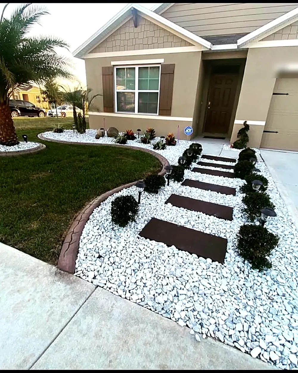 Finished front yard with white rock beds, stepping pavers, and trimmed shrubs